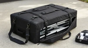 A folded black portable massage table secured with straps and packed into a canvas carrying case with shoulder straps for mobile massage therapists.